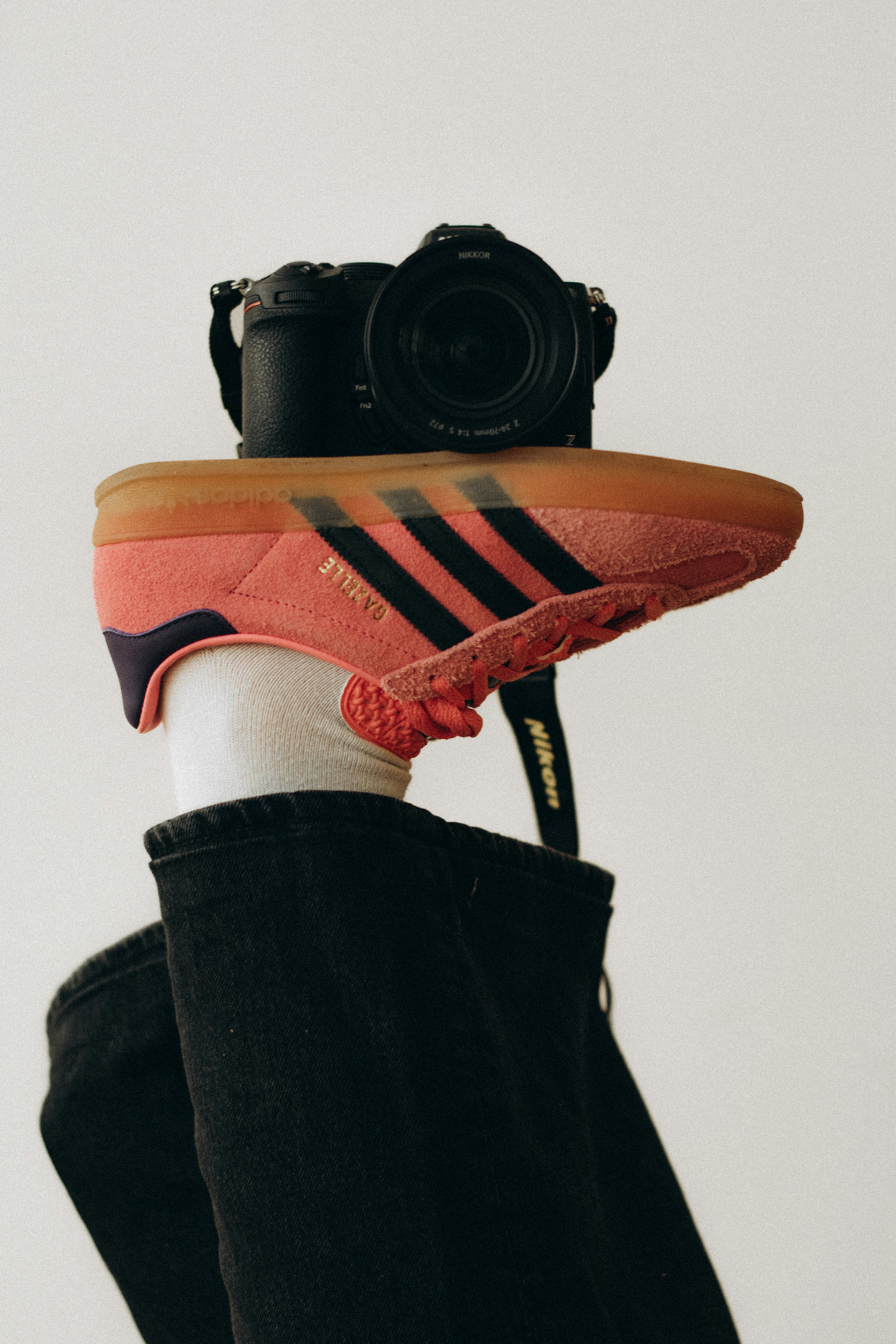 Pink adidas sneaker balanced on a camera lens.