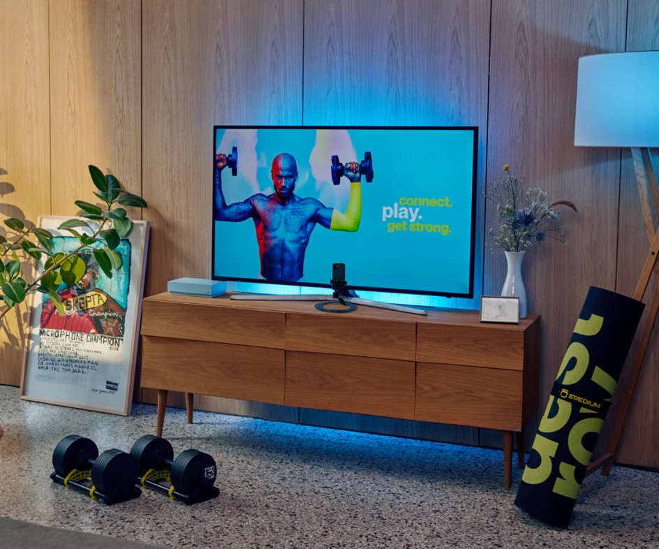 Staedium strength gaming setup with big screen and adjustable dumbbells.