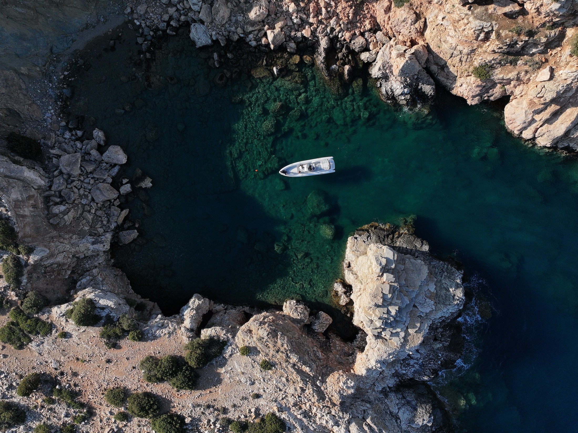 White motor yacht anchored in crystal-clear turquoise waters beside dramatic limestone cliffs and rocky coastline in the Cyclades.