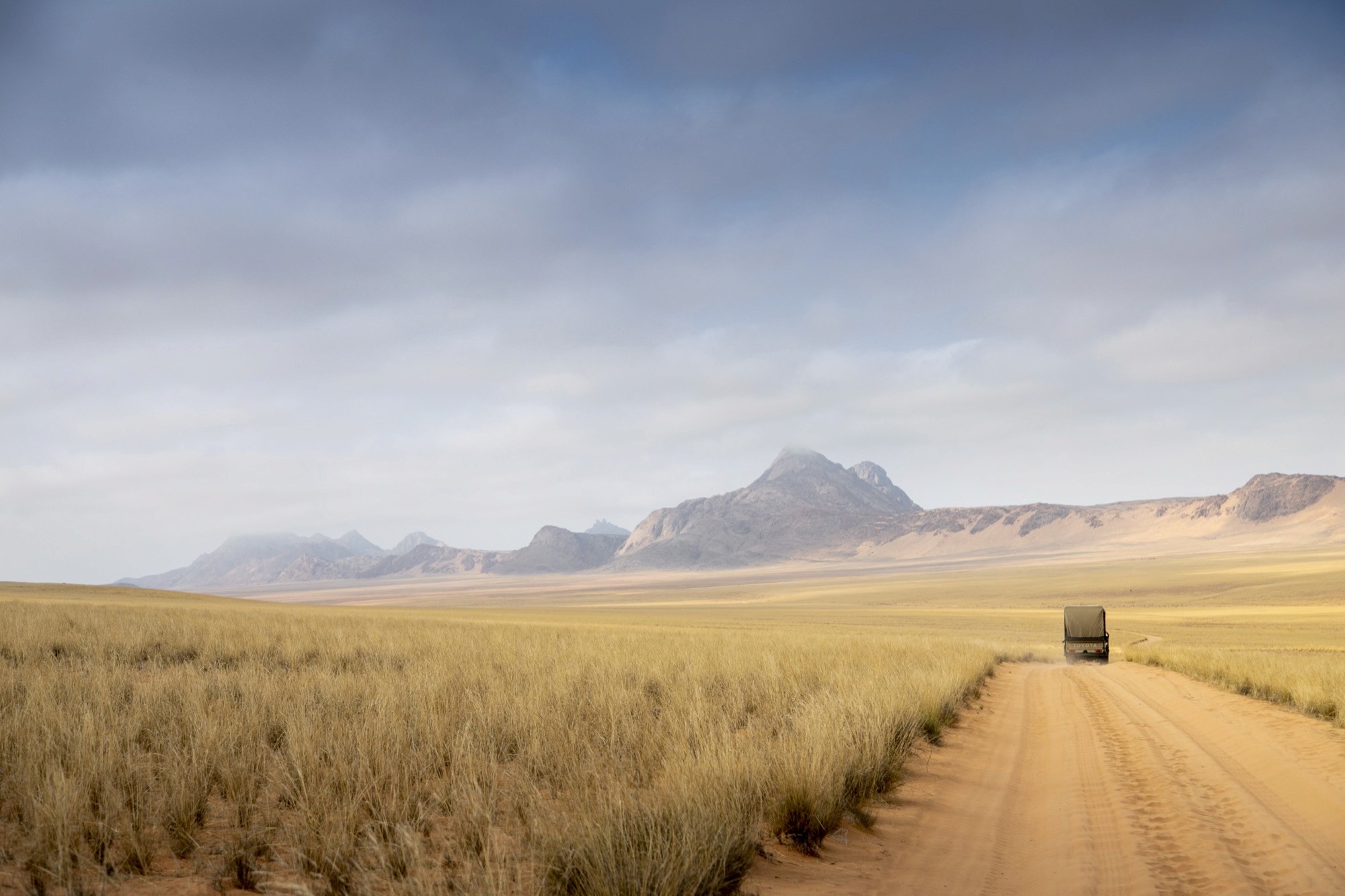 A single vehicle on an empty gravel road running toward distant desert mountains