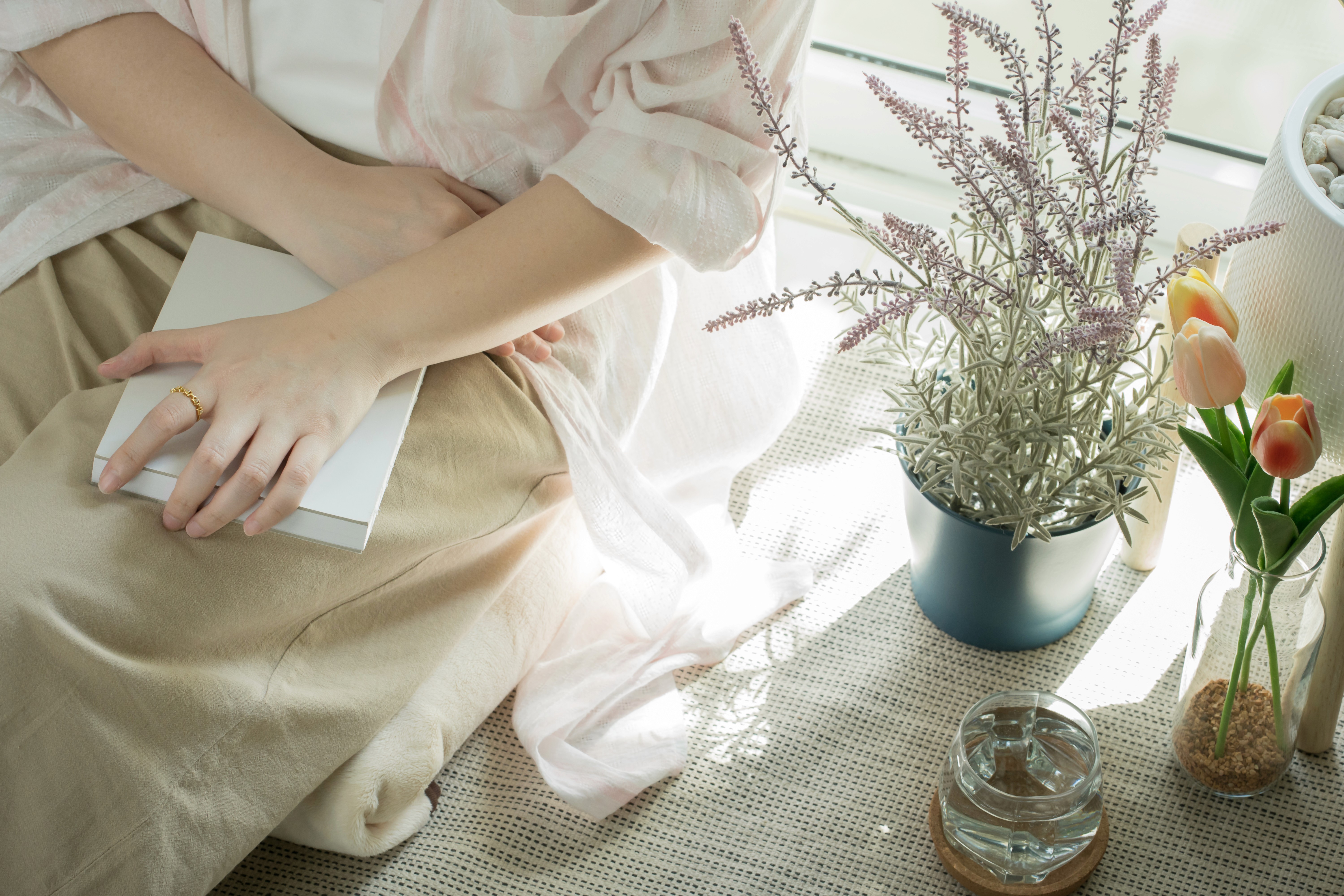 Vrouw in lichte kleding met een notitieboek op schoot naast een plant, symbool voor de zoektocht naar antwoorden op hormonale klachten.