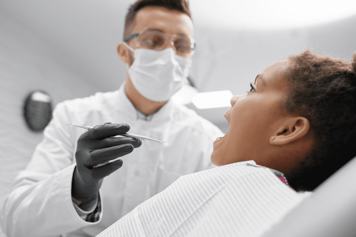 A dentist wearing a mask and gloves holding dental tools while examining a patient's teeth.