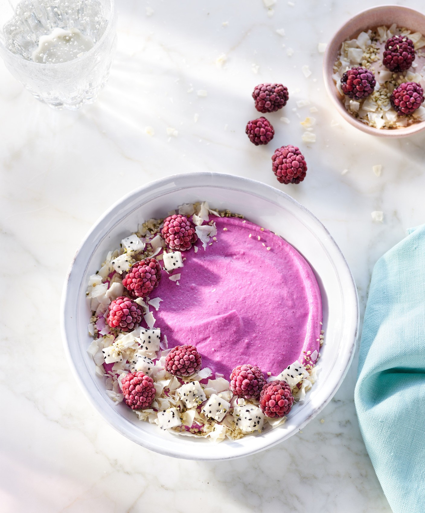 Styled pink smoothie bowl garnished with cubes of dragonfruit, frozen raspberries, coconut flakes, and sesame seeds.
