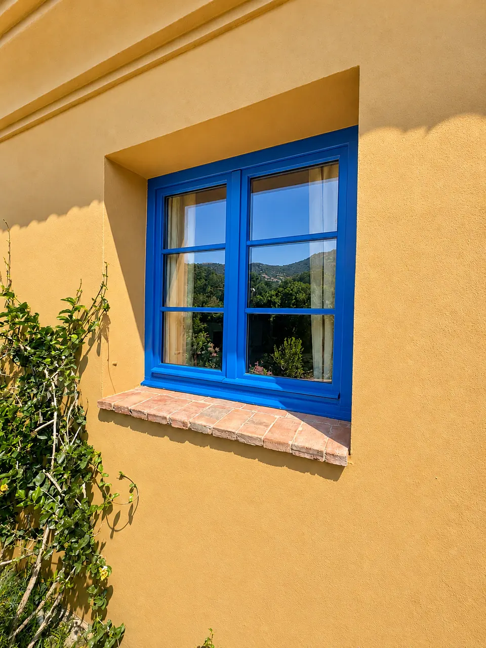 Fenêtre en bois bleu sur la façade ocre de la maison de San Damiano, avec appui en terre cuite