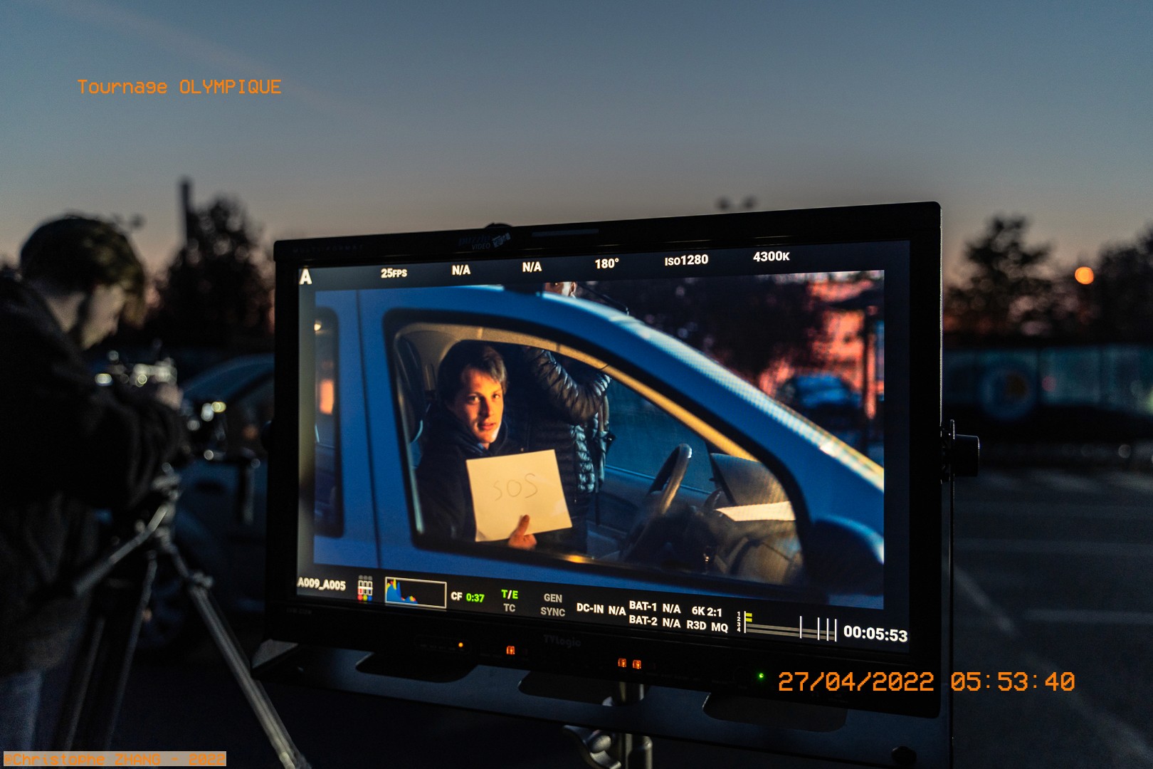 Moniteur affichant un acteur en voiture, tenant un message "SOS" pendant une prise nocturne.