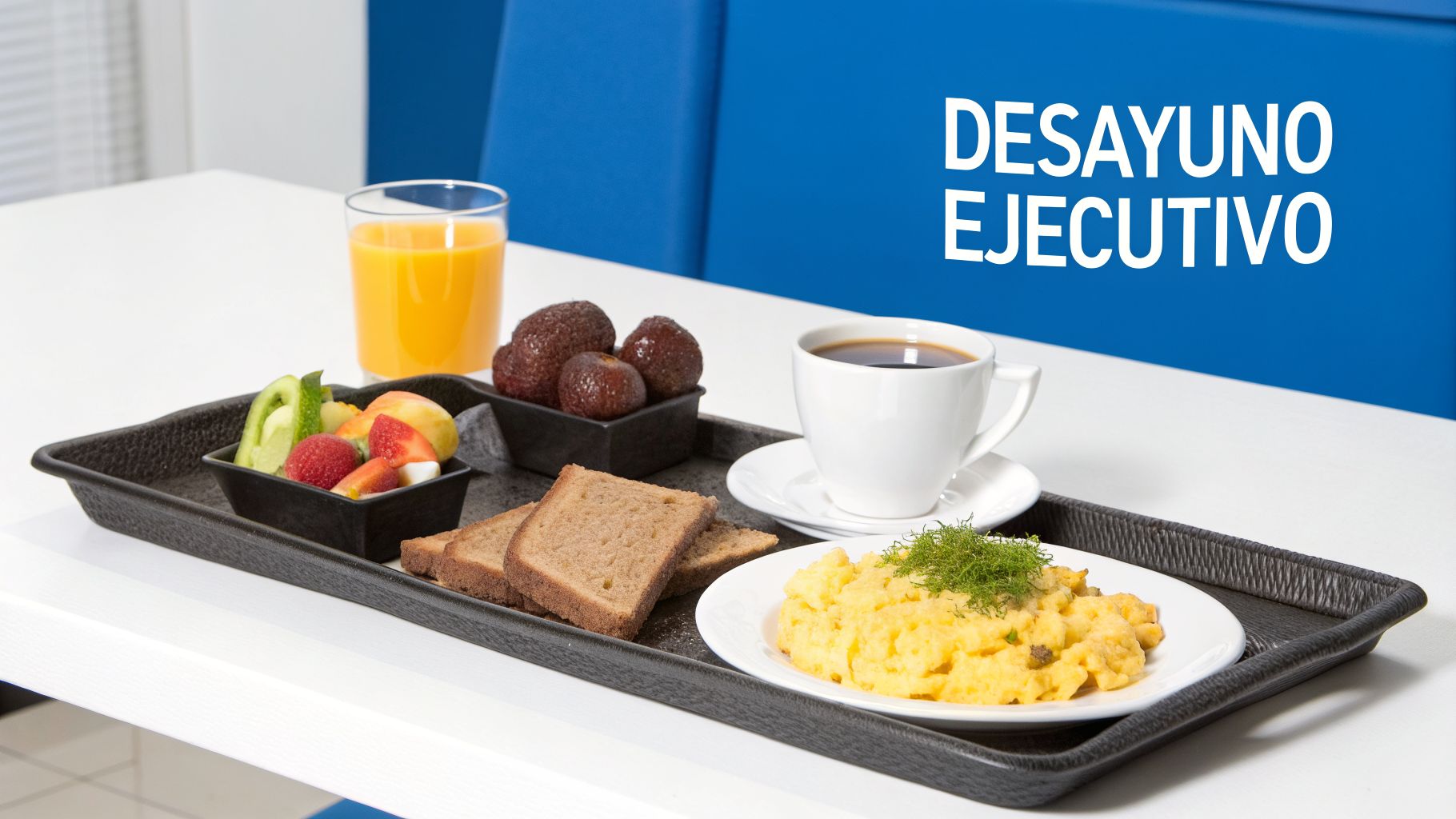 Un desayuno ejecutivo en una bandeja oscura, incluyendo jugo de naranja, café, fruta fresca, huevos revueltos y tostadas de pan integral.