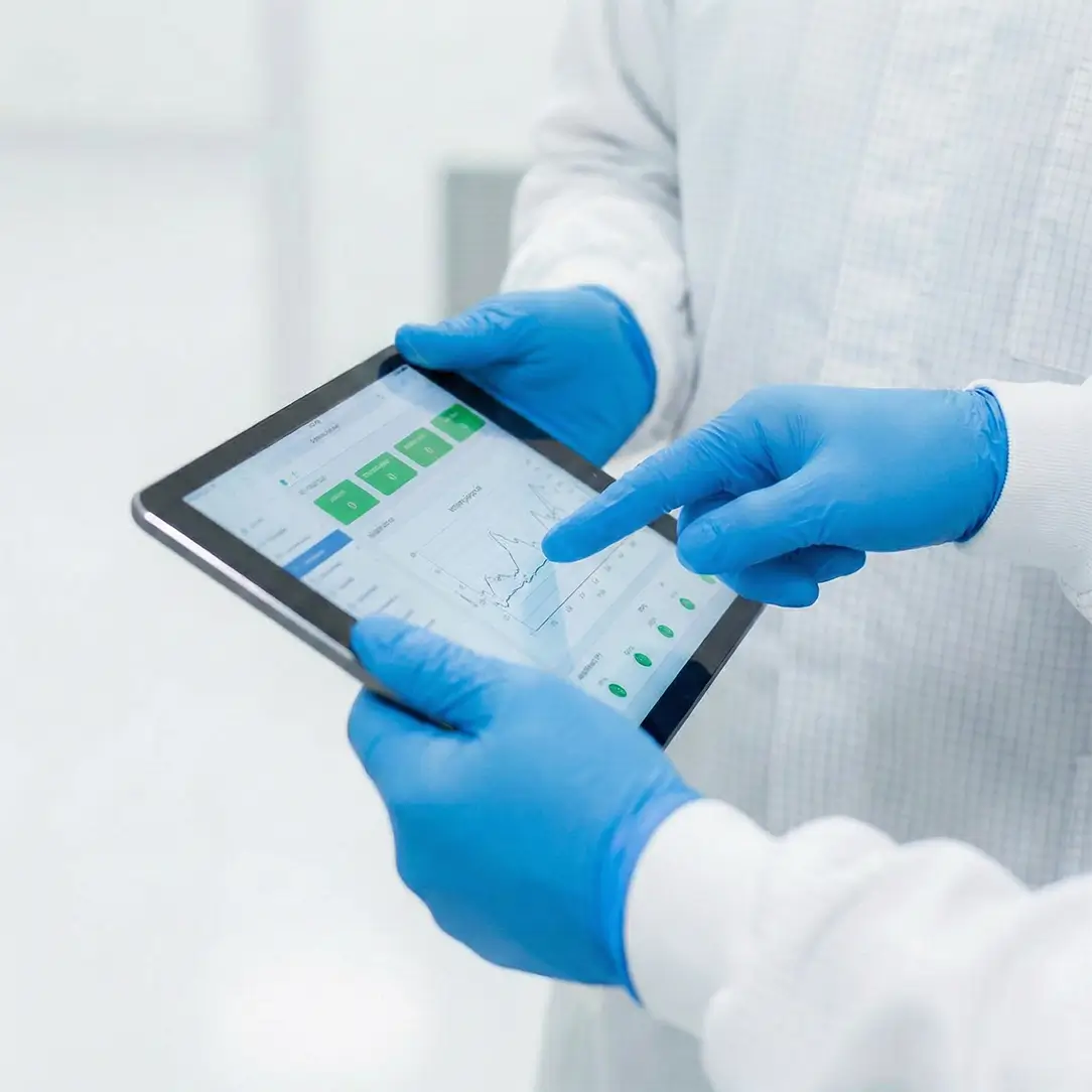 Two pharmaceutical professionals in cleanroom attire working side-by-side, monitoring real-time production batch data on a digital tablet during a facility ramp-up phase.