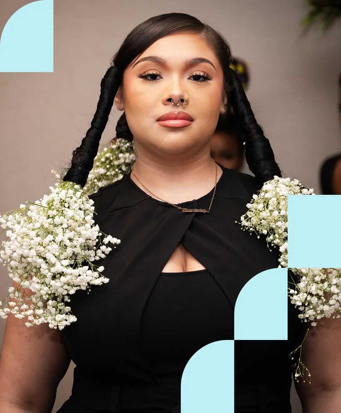 A woman with an intricate hairstyle featuring long braids adorned with white baby's breath flowers. She wears a black dress with a confident expression. Blue geometric shapes frame the image.