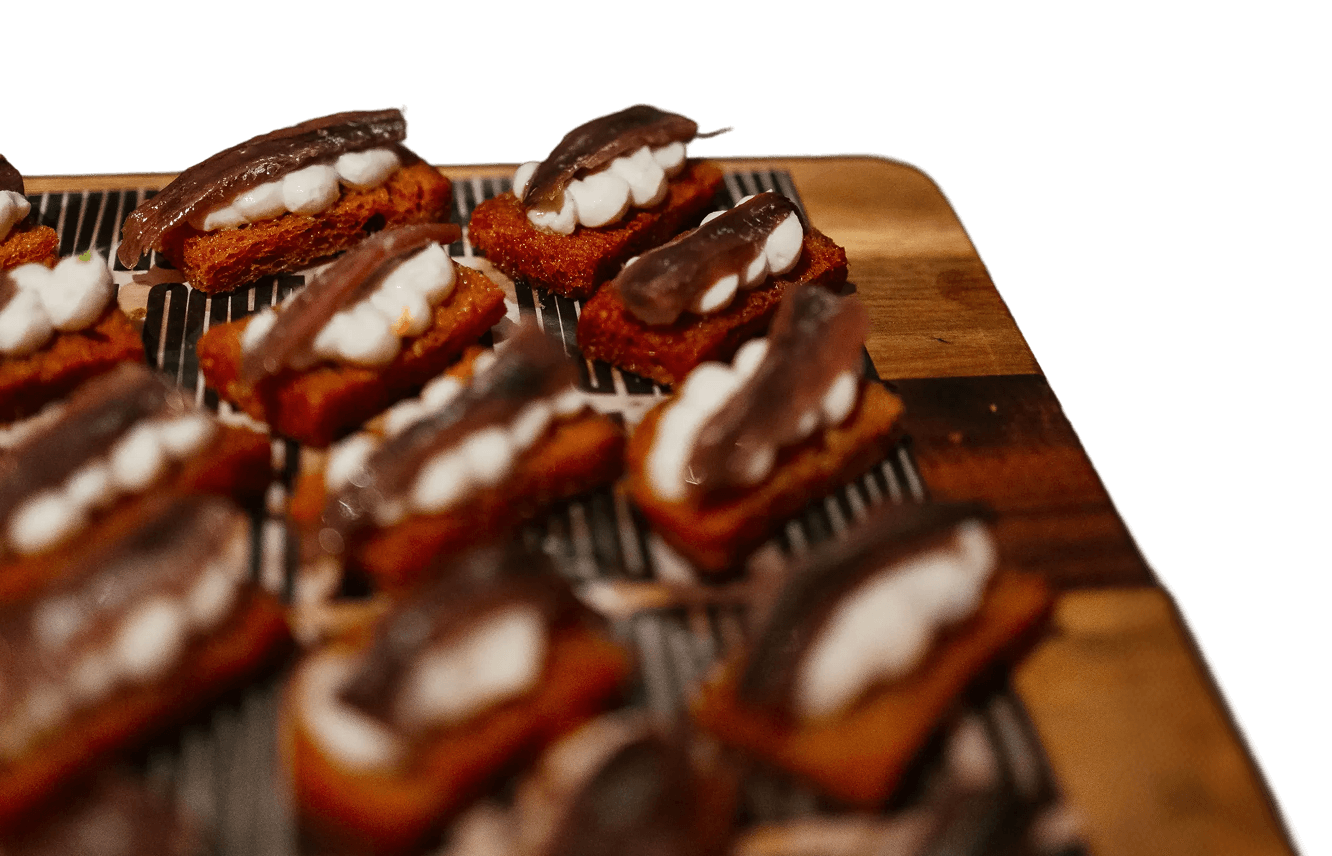 Primer plano de aperitivos gourmet con anchoa sobre pan especiado servidos en una tabla de madera