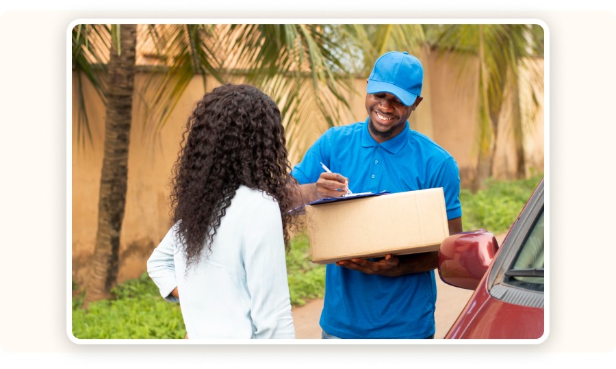 Livreur souriant en tenue bleue remettant un colis à une cliente et lui faisant signer un bordereau de livraison, illustrant le dernier maillon de la chaîne logistique dans l’e-commerce.