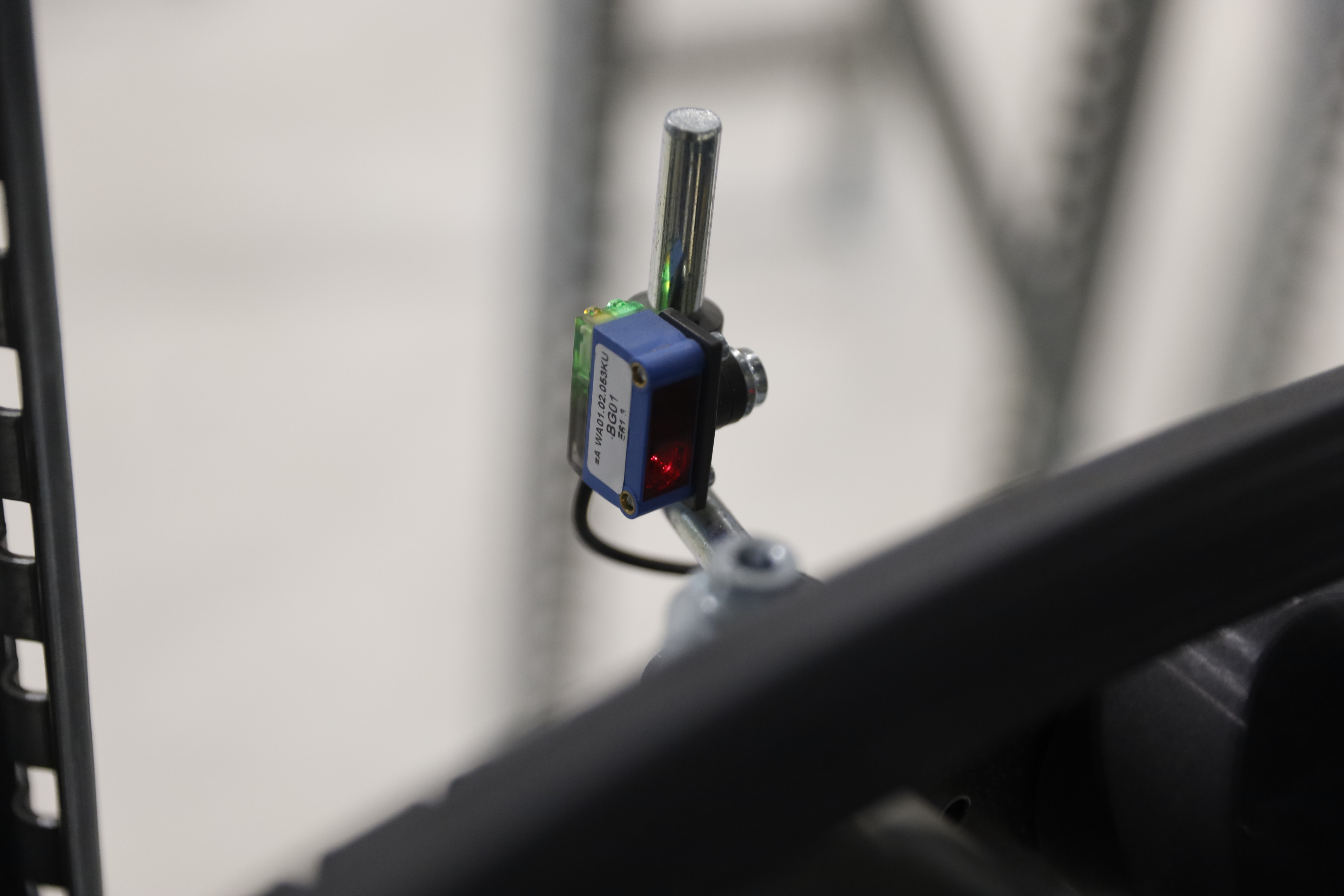 Närbild av en maskinsensor med rött ljus som indikerar aktivitet. Metallrör och elektroniska komponenter syns.