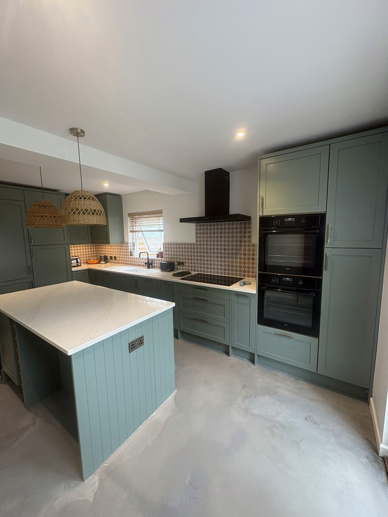 Finished kitchen with sage-green cabinets, a central island, pale worktops and built-in ovens.