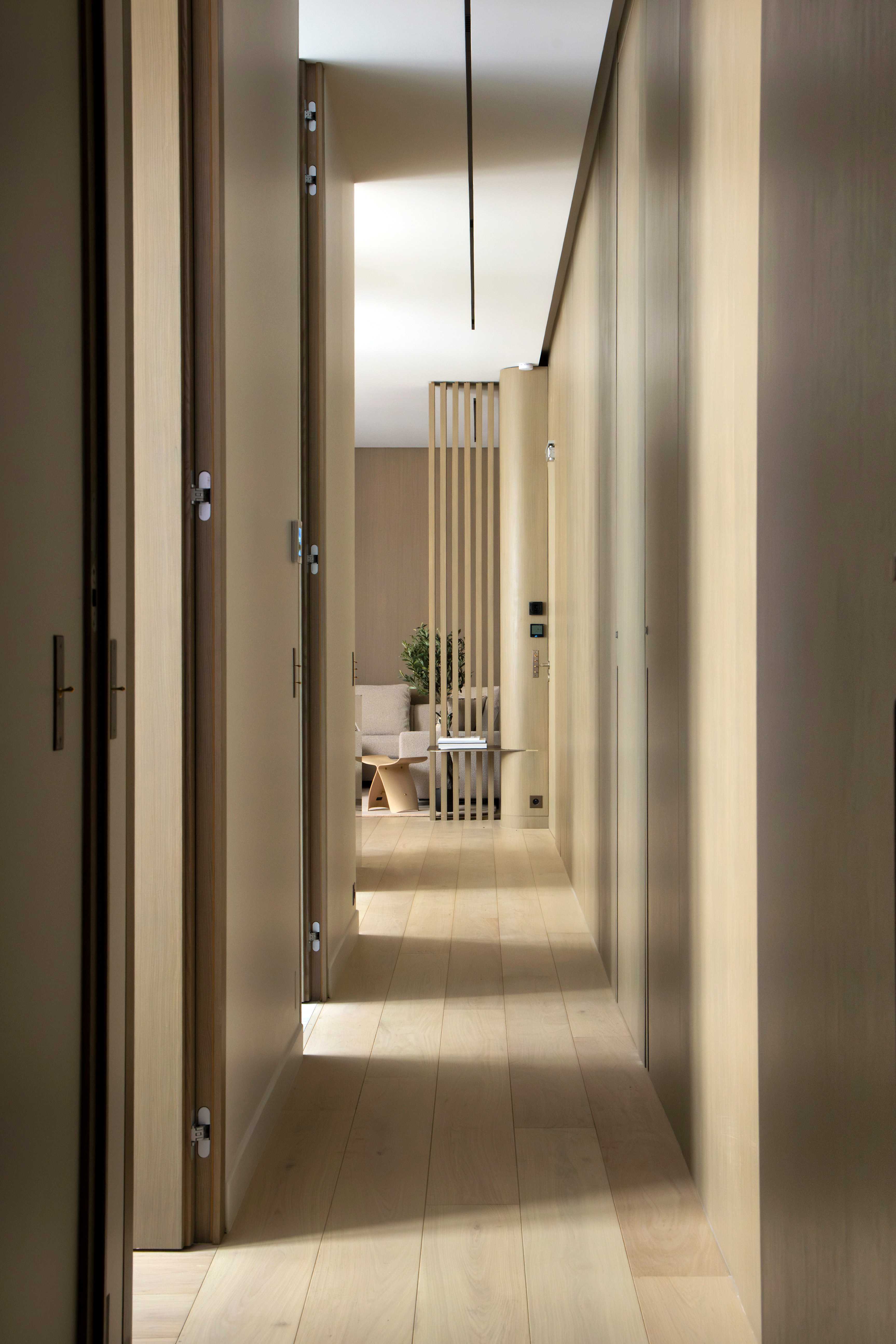 Couloir de l'appartement en bois clair avec parquet, claustra, perspective sur le salon et suspension noire