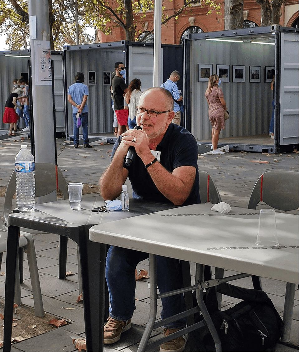 Frédéric Bourcier, photographe documentaire, s’exprime au micro lors d’une rencontre publique autour de son exposition photo installée dans des conteneurs urbains.