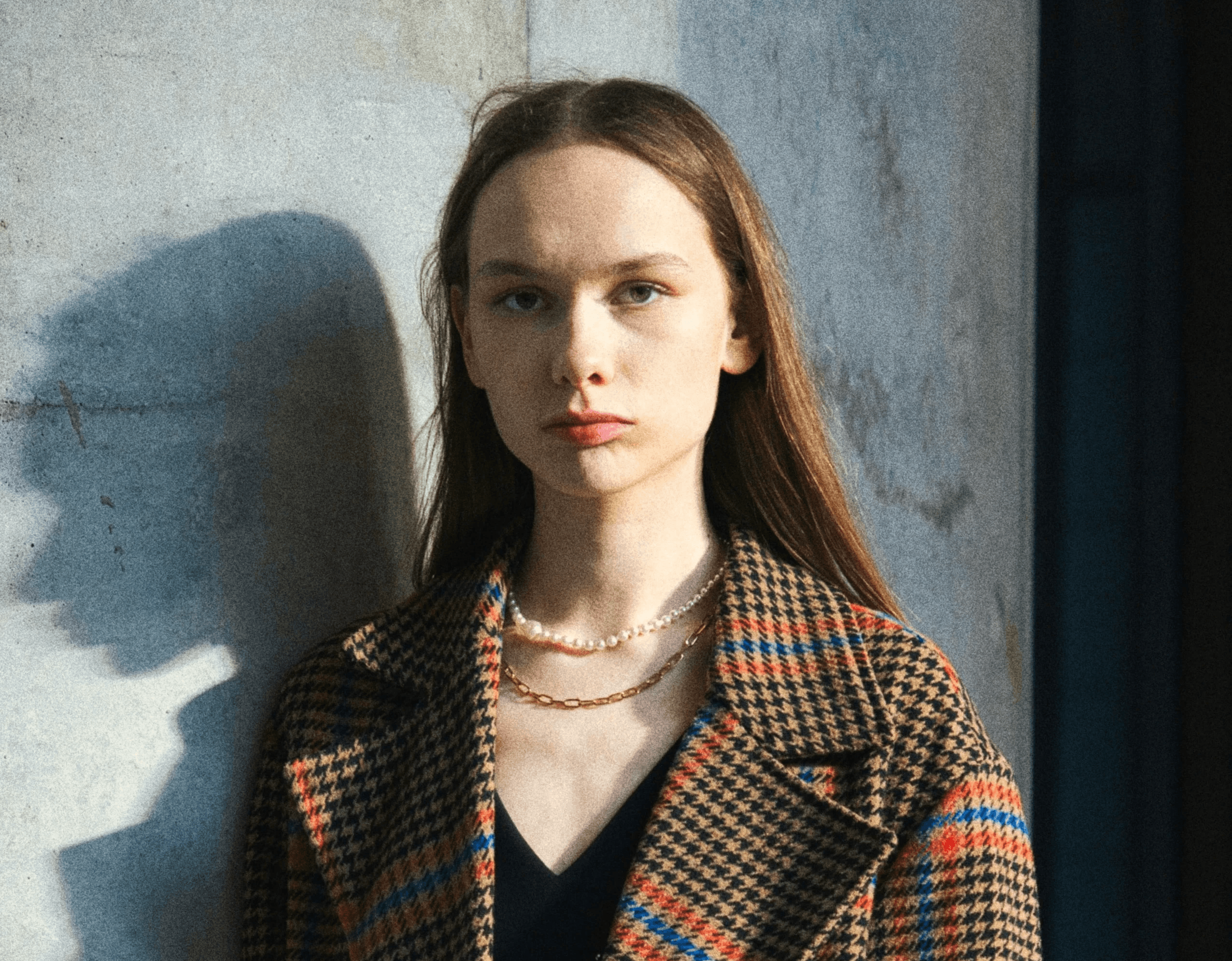 Woman in plaid coat stands by concrete pillar
