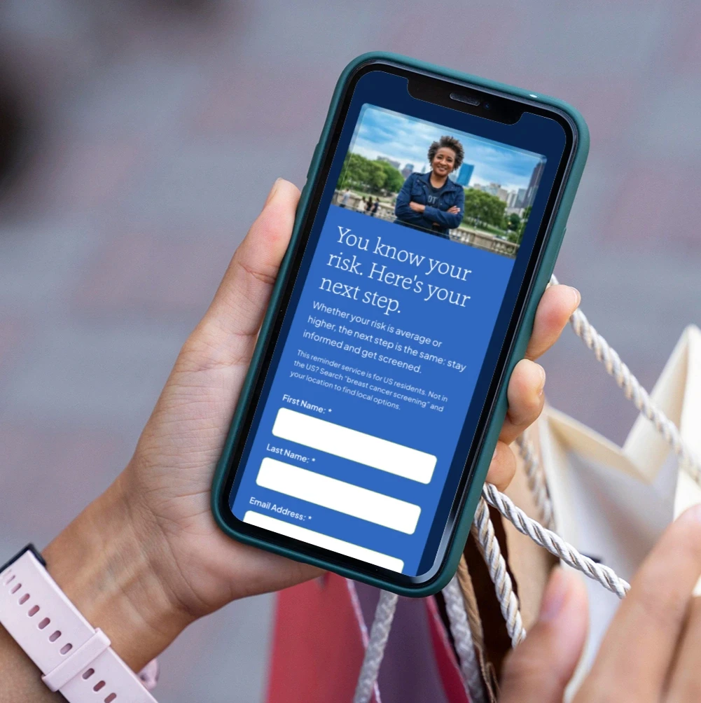 A person holding a mobile phone displaying a sign-up form for a screening reminder, titled 'You know your risk. Here's your next step.'