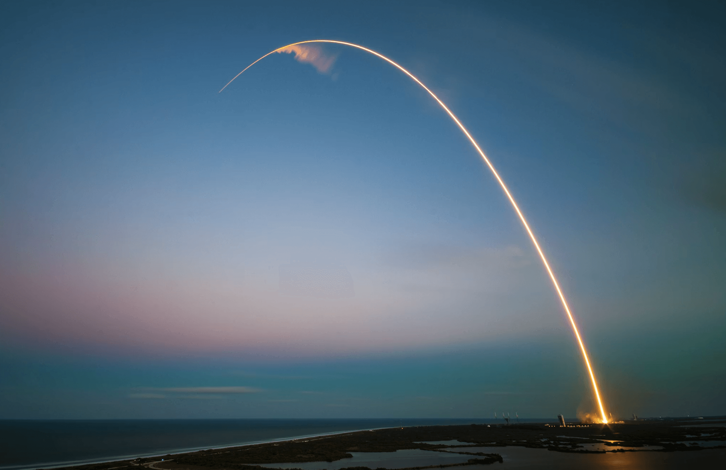 A winding road cuts through rocky terrain, surrounded by patches of green grass and illuminated by sunlight.