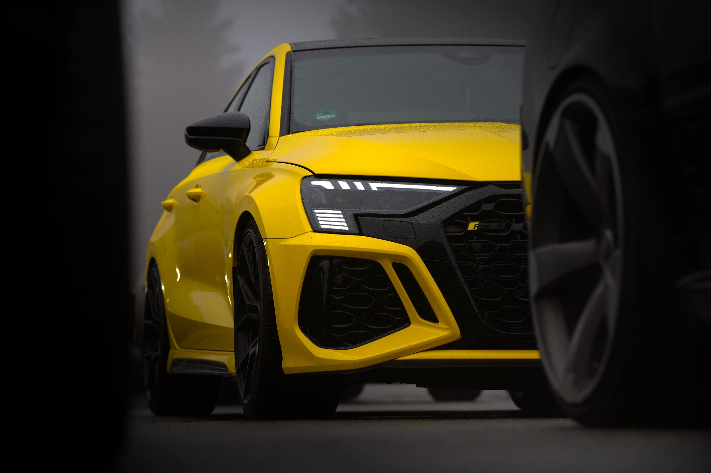Audi RS3 in Pythongelb beim Audi RS Treffen Crottendorf 2025, aufgenommen aus einer kreativen Perspektive zwischen anderen parkenden Audis.
