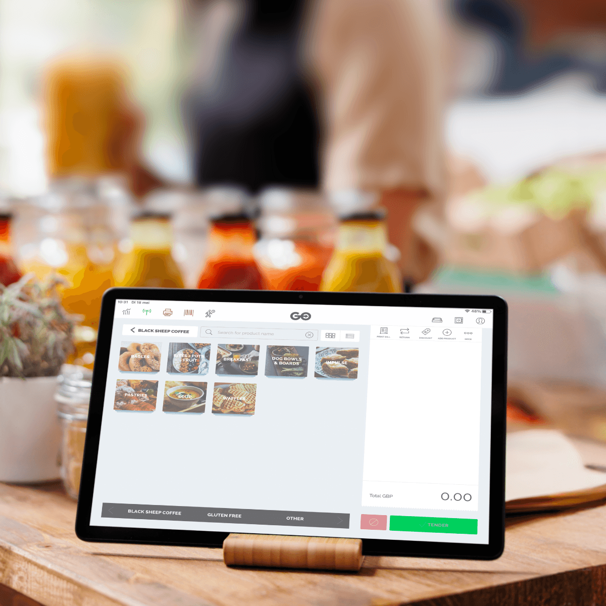 A young person with curly hair smiles at the camera while sitting in front of a laptop against a dark background.