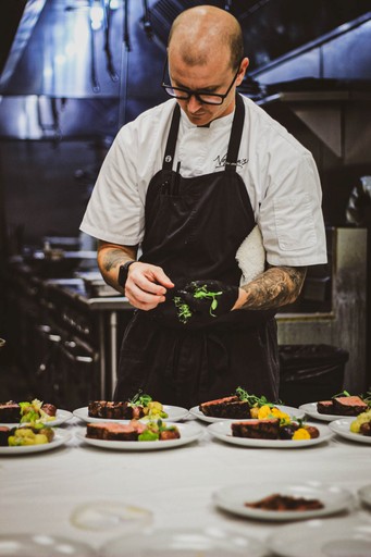 Chef carefully plating a gourmet meal of sliced beef, mashed potatoes, and green garnish.