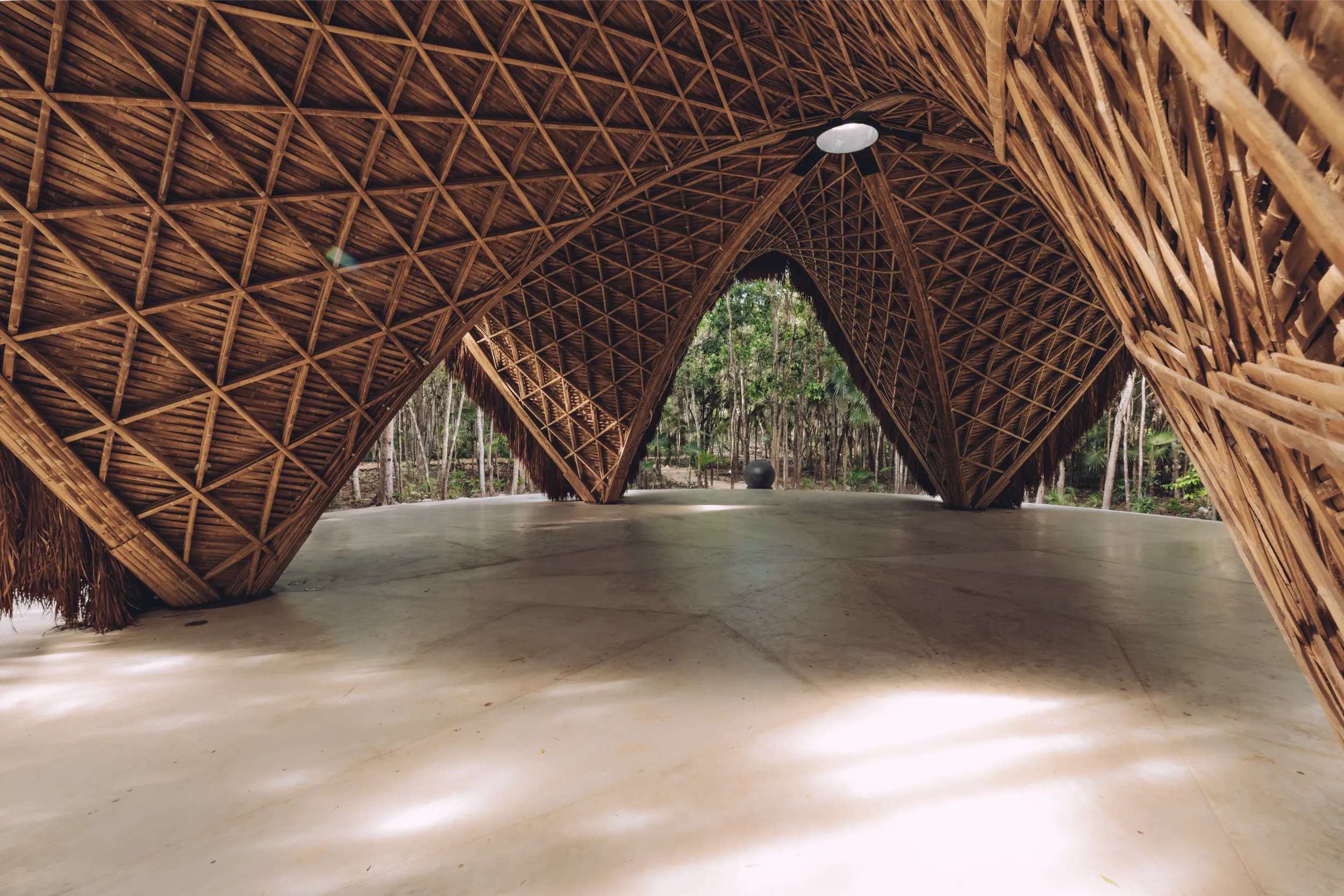 Wide interior view of Luum Temple, showcasing the sweeping bamboo arched vaults and the open-air connection to the surrounding forest.