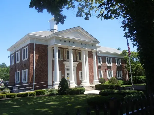 A stately brick building with white columns, surrounded by greenery and a clear blue sky.