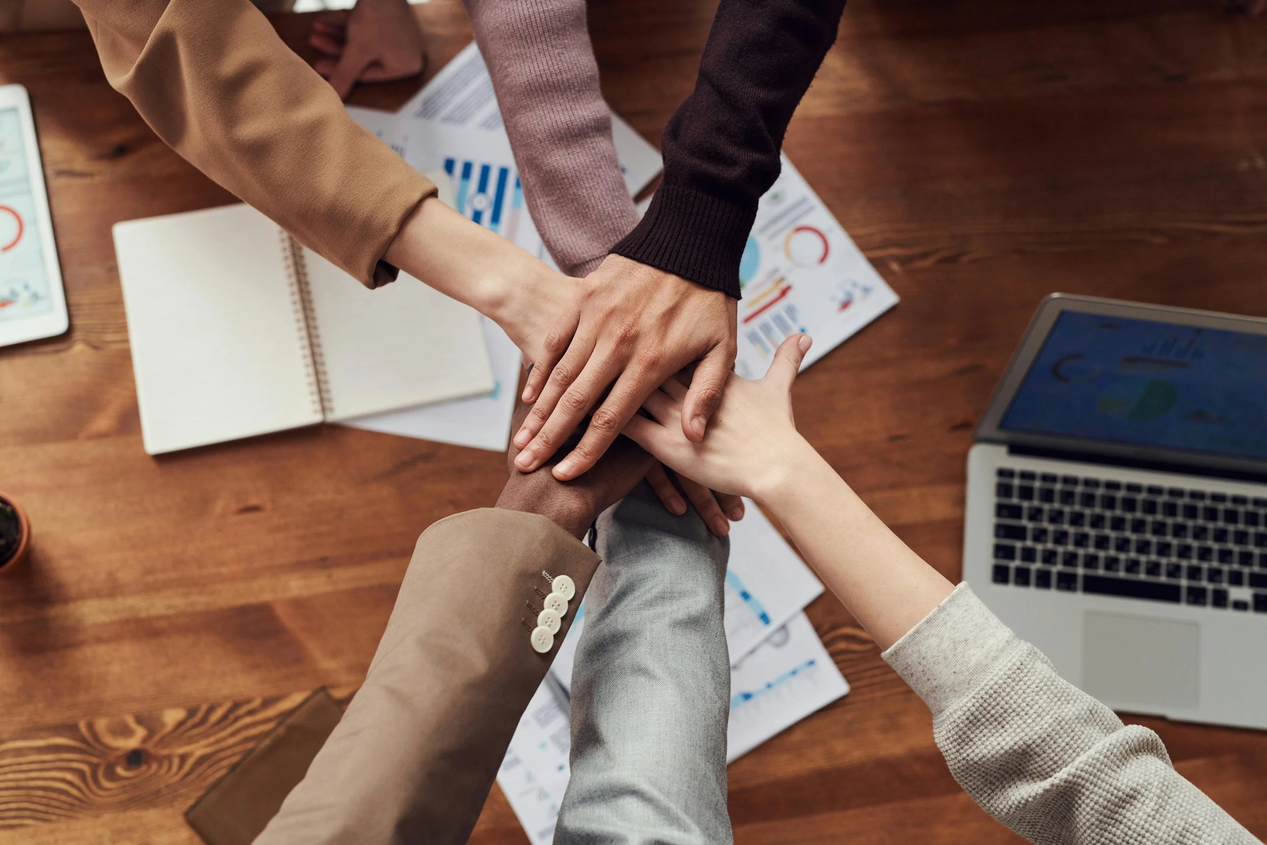 A diverse team placing their hands together over a table during a collaborative planning session.