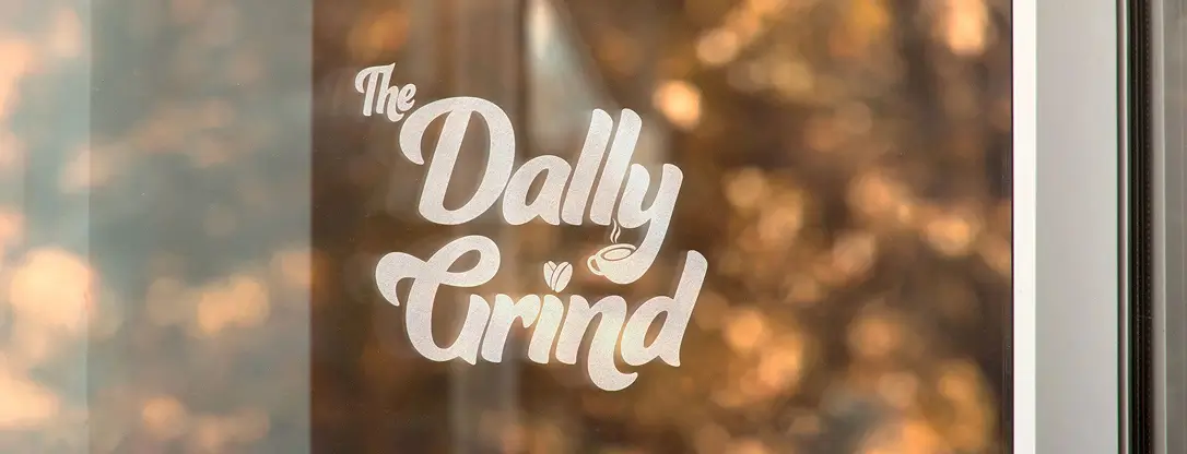 The Dally Grind logo in white custom script over a warm, blurred background, showcasing branding application.