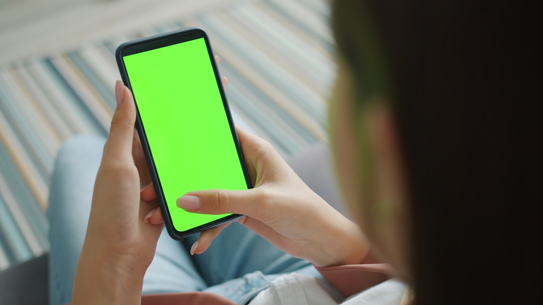Person holding a smartphone with a green screen.