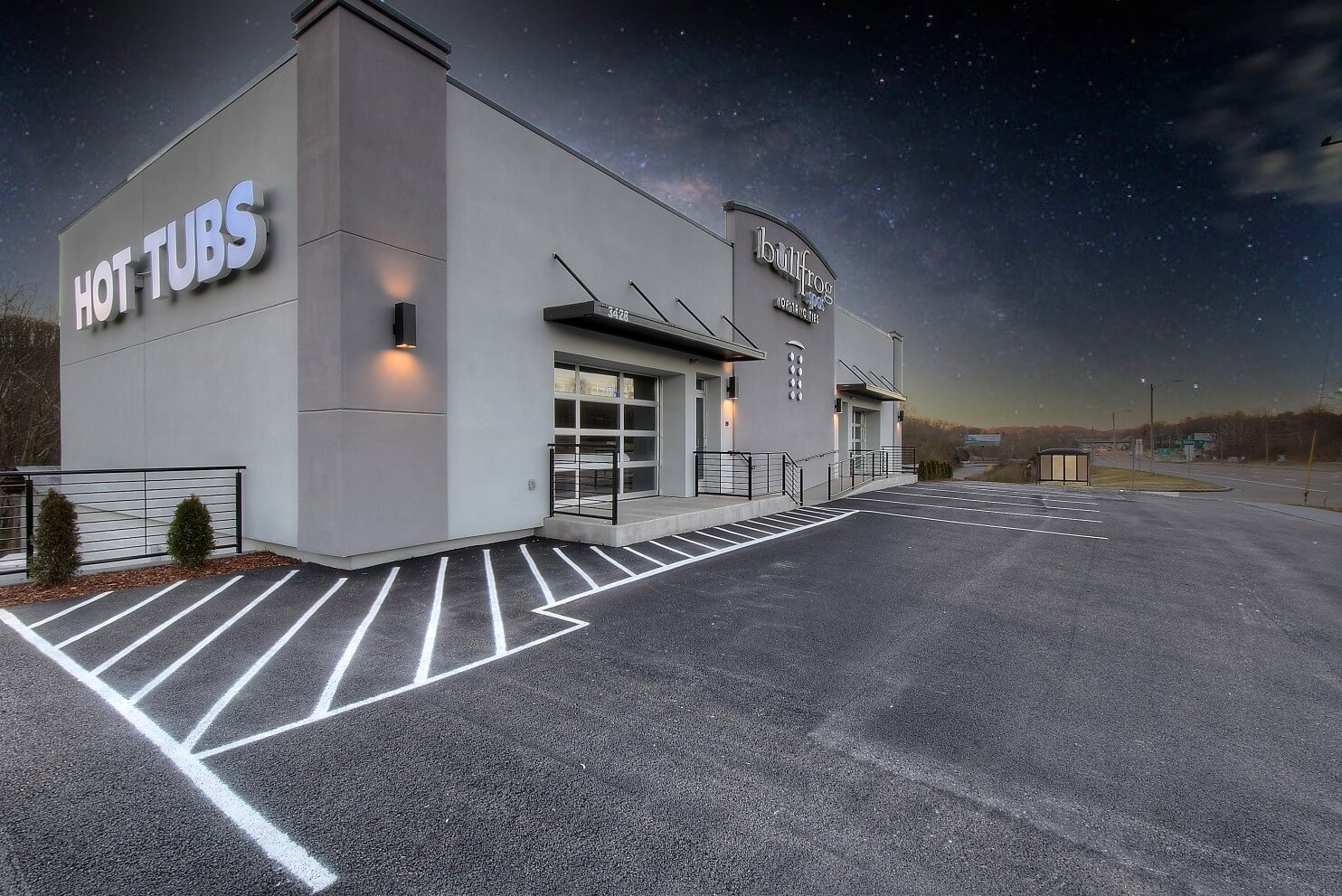 A modern building with a large entrance and parking area, set against a dark, cloudy sky.