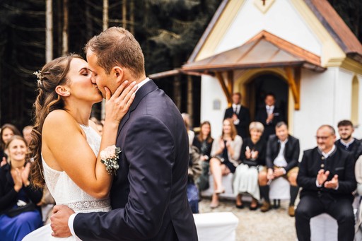 Brautpaar küsst sich nach der Trauung vor Gästen bei Hochzeit im Freien vor Kapelle