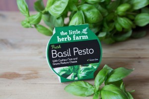A close-up image of our basil and pesto product. Green packaging surrounded by fresh basil 