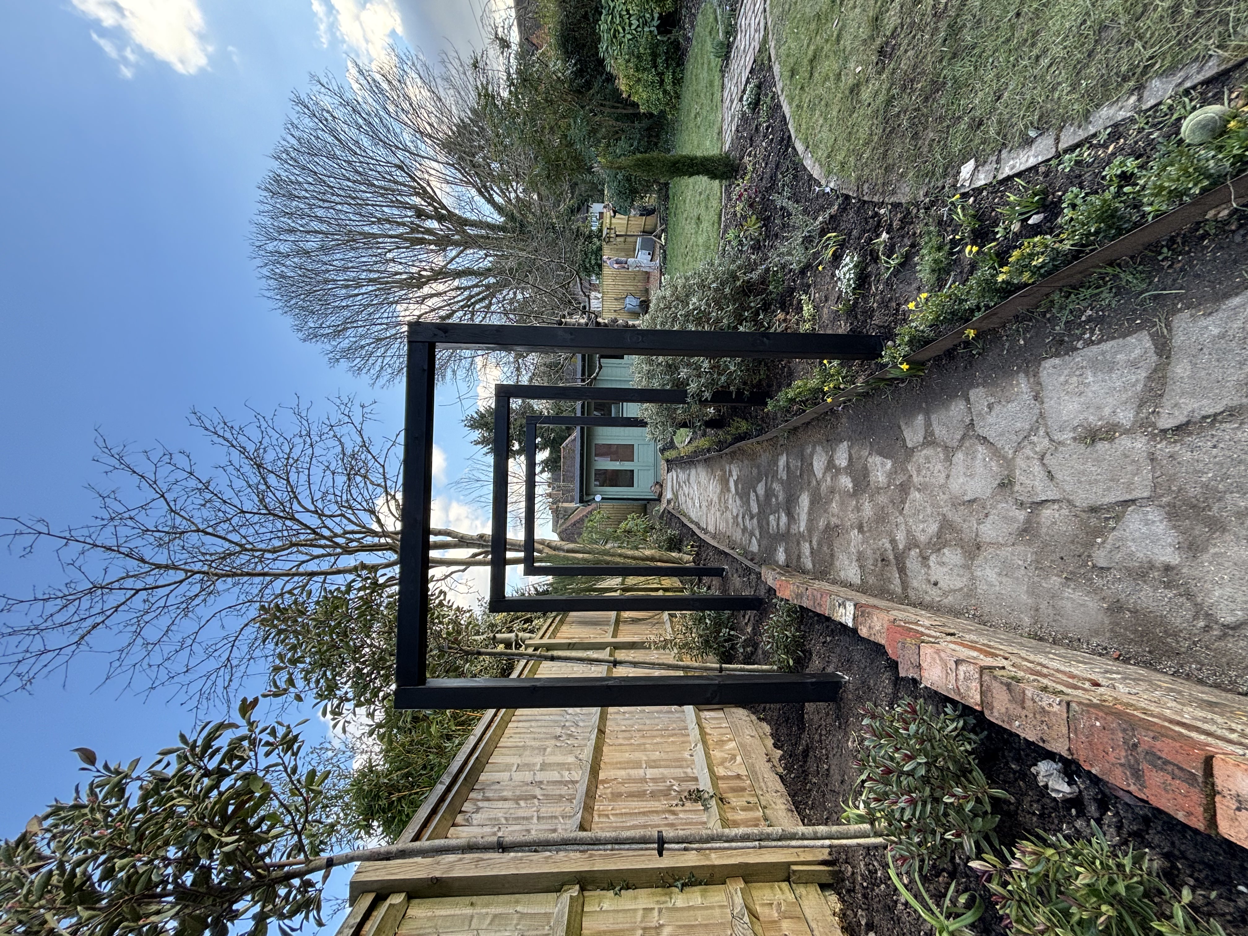 "Natural stone pathway lined with multiple decorative black metal garden arches in Marlow