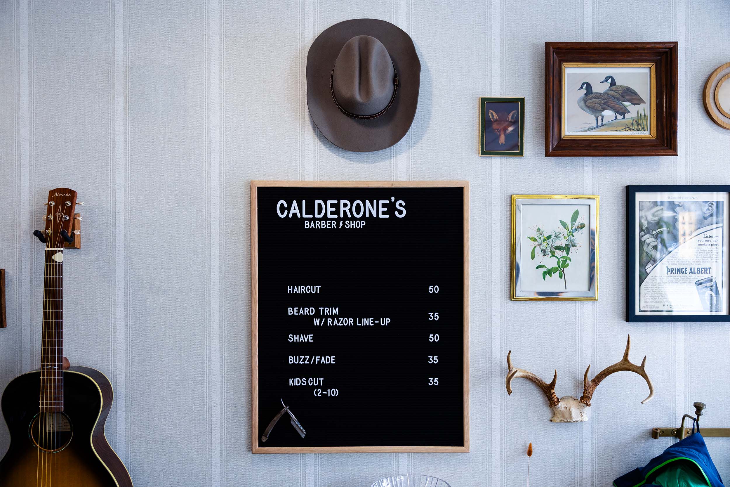 Interior wall display at Calderone’s Barbershop featuring framed artwork, decor, and the service menu board