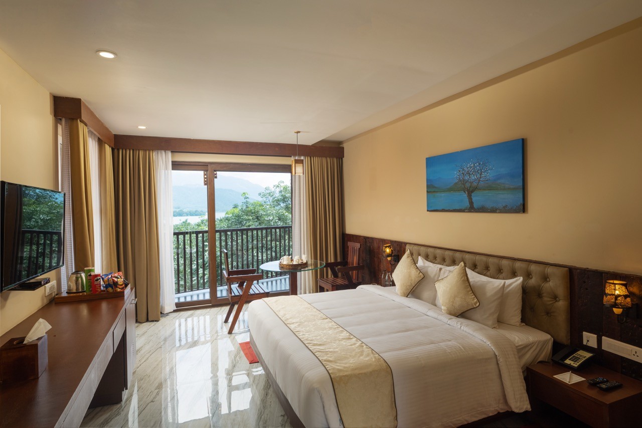 Luxurious room interior at Au Revoir Resort, featuring a cozy king-size bed, elegant decor, and a private balcony with a stunning nature view