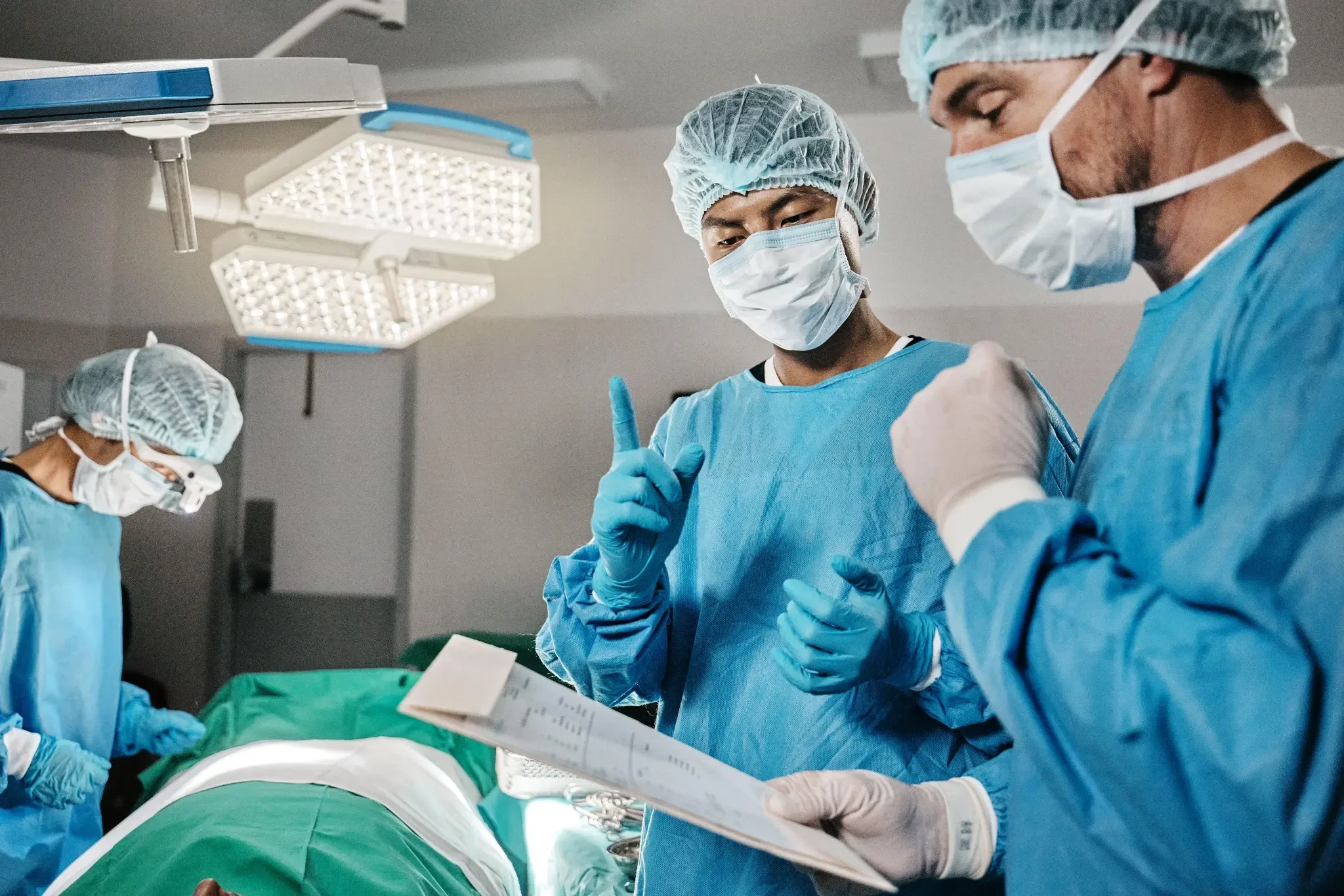 Surgical team in blue scrubs and protective masks communicating in an operating room.