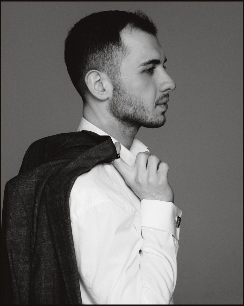 Black-and-white profile portrait of a man adjusting his white shirt collar
