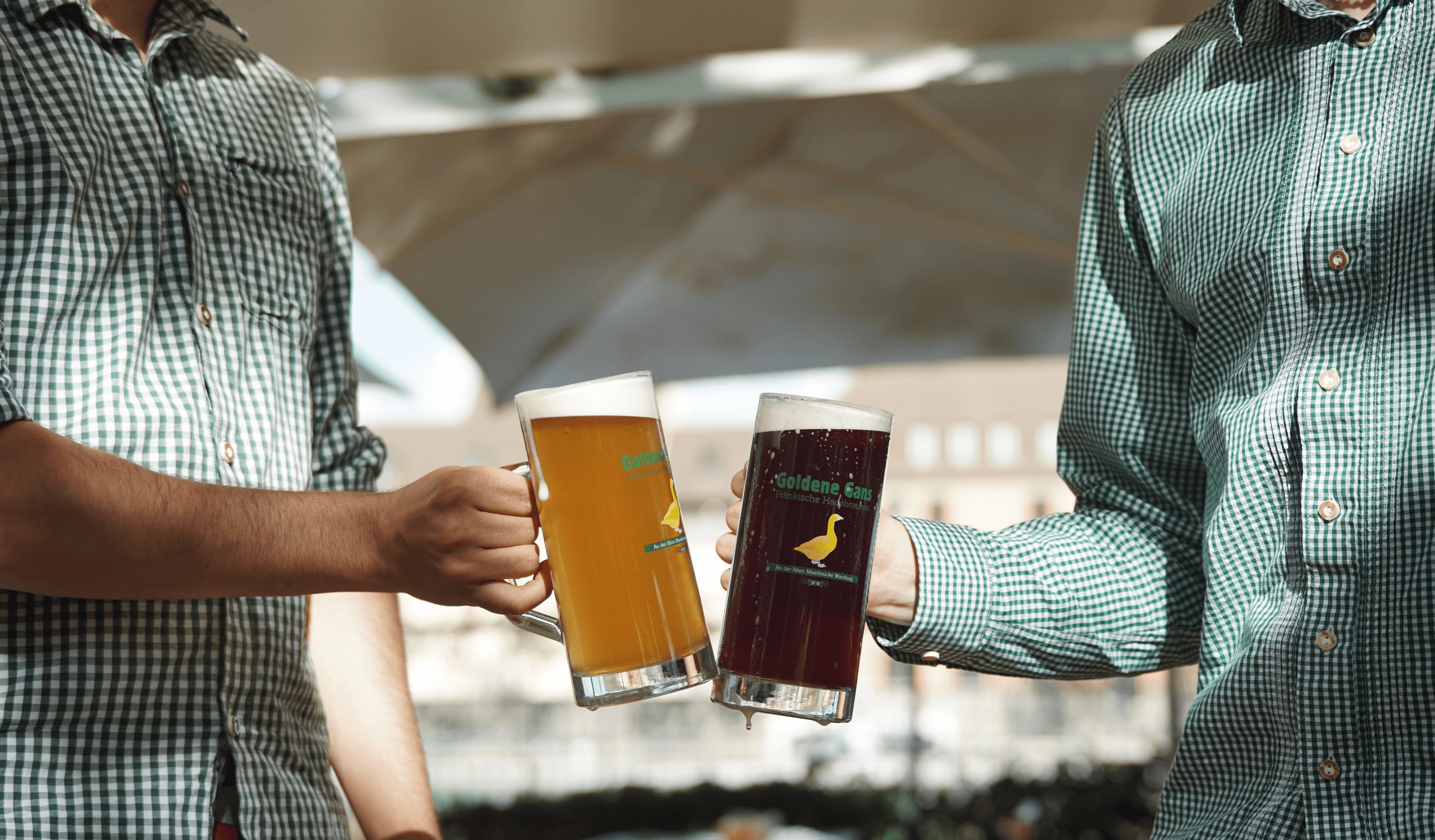 Zwei Personen stoßen mit großen Bierkrügen, helles und dunkles Bier, an. "Goldene Gans" Logo auf den Krügen