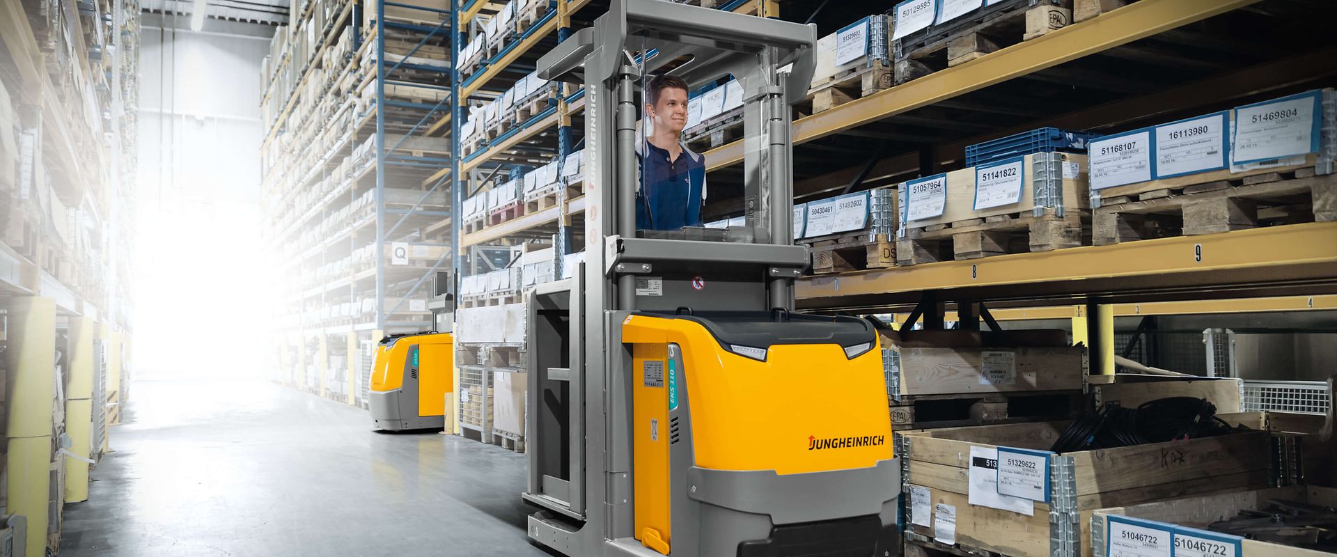 Two people in a workshop, one standing and smiling while the other leans over a car, working on it.