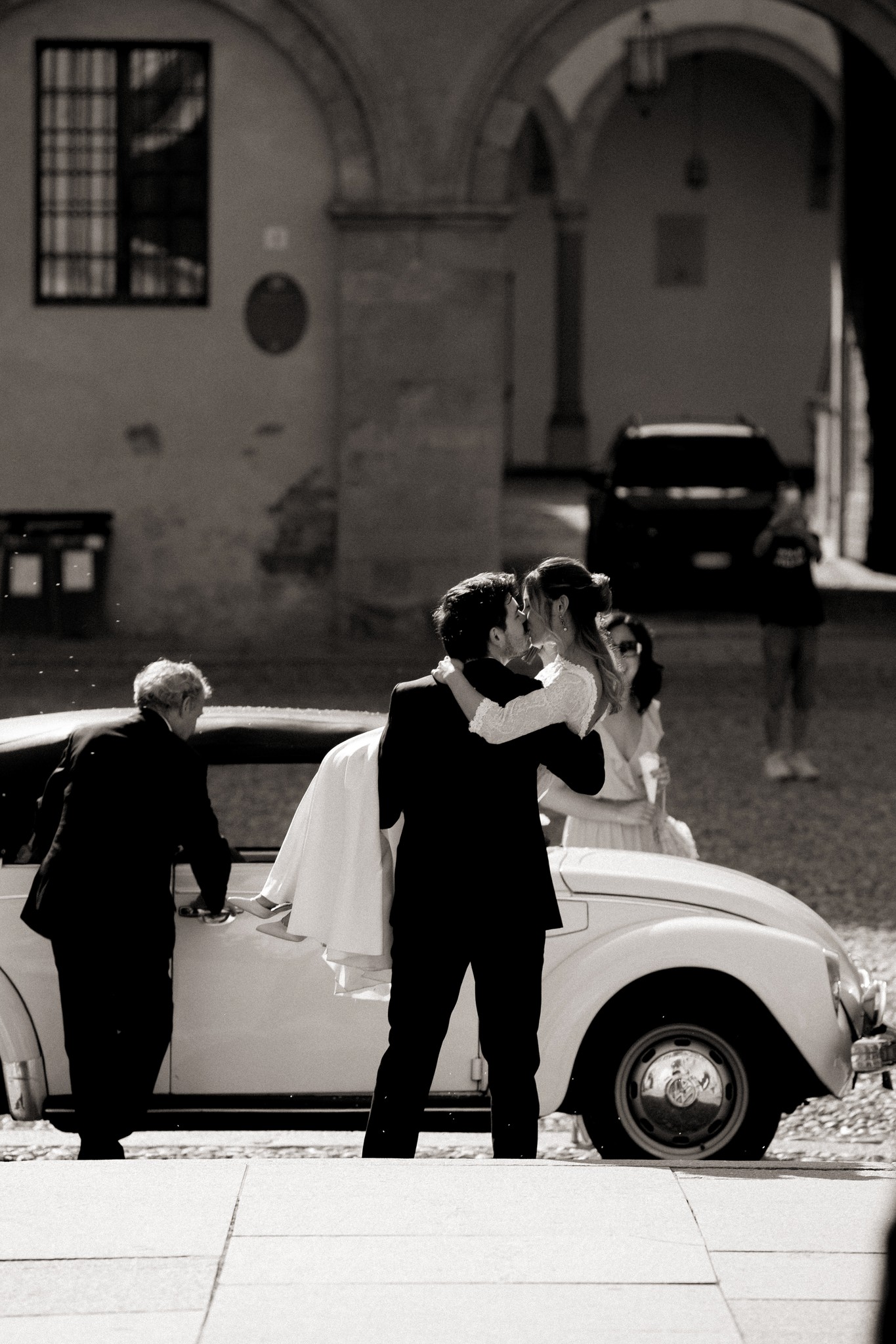 Matteo solleva Francesca al portale di Villa Peroni Riva dopo la cerimonia, il Maggiolino bianco sullo sfondo del matrimonio