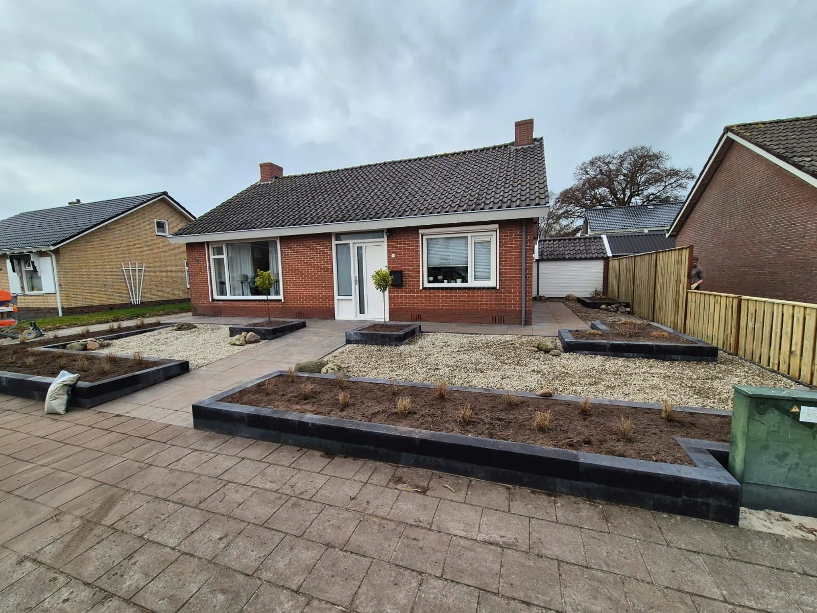 Rustige, onderhoudsarme voortuin met grind, verhoogde plantvakken en bestrating voor een bakstenen huis in Harkema.