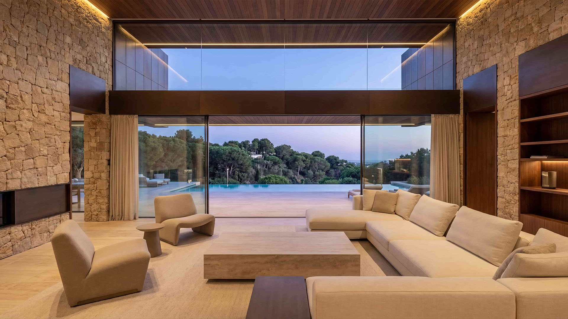 Modern villa living room with stone walls and open view toward the terrace at dusk