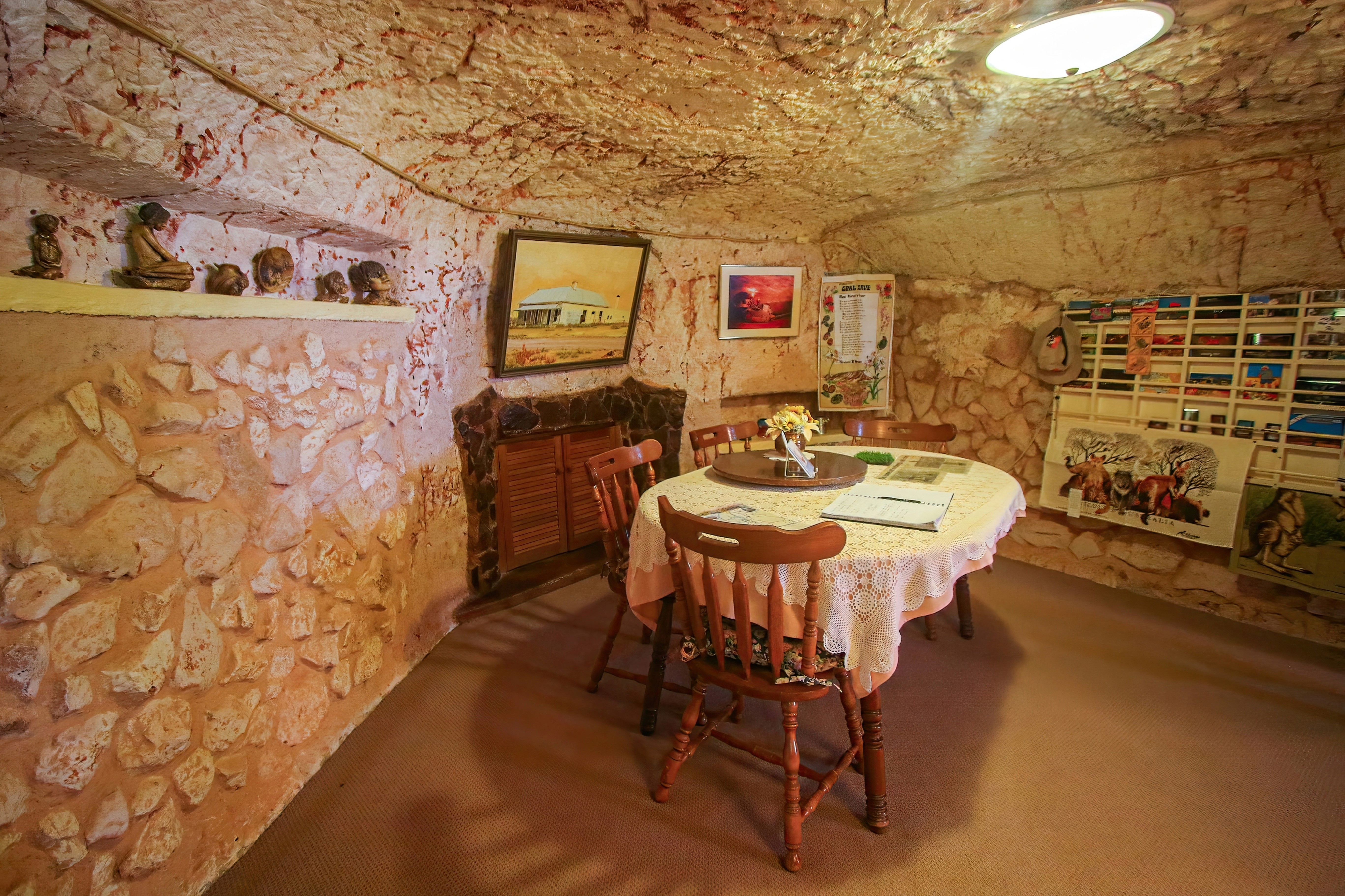 The interior of an underground home in Coober Pedy, Australia, featuring a cozy dining area with a round table, stone walls, decorative art, and subdued lighting