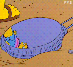 Lisa Simpson in a tie-dyed shirt, cap, and granny glasses looking at her reflection in a discarded Jiffy Pop container