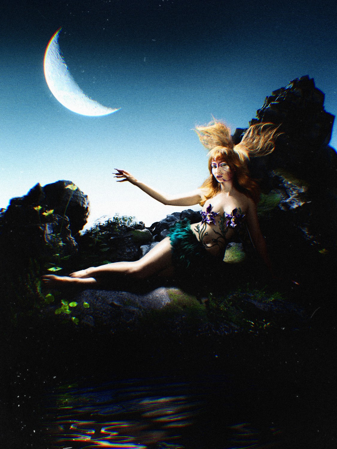 Conceptual fine-art photograph by Lélio Bazin for DramatK, depicting an ethereal mermaid-like figure resting on dark, mossy rocks under a large crescent moon, featuring flowing red hair, hand-painted body art, and natural elements, with a textured, painterly finish against a clear blue sky.
