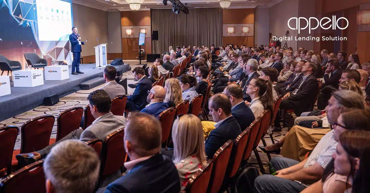 A large audience attentively listening to a speaker at an Appello Digital Lending Solution conference, featuring a professional presentation setting.