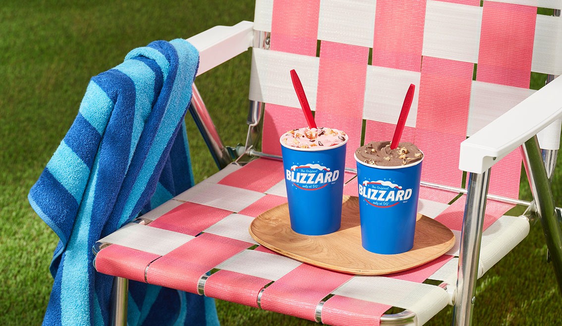 WTADS client DQ two Blizzards in blue cups sitting on retro pink chair with blue beach towel in grass.