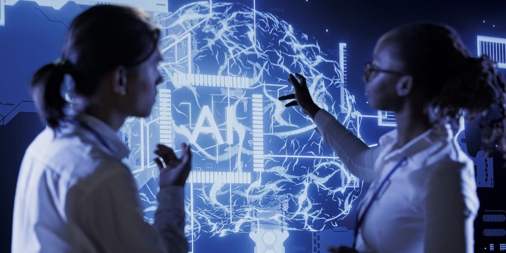 Two diverse professionals, a man and a woman, standing in front of a large, glowing blue digital brain interface with the letters 'AI' at the center of a neural network display