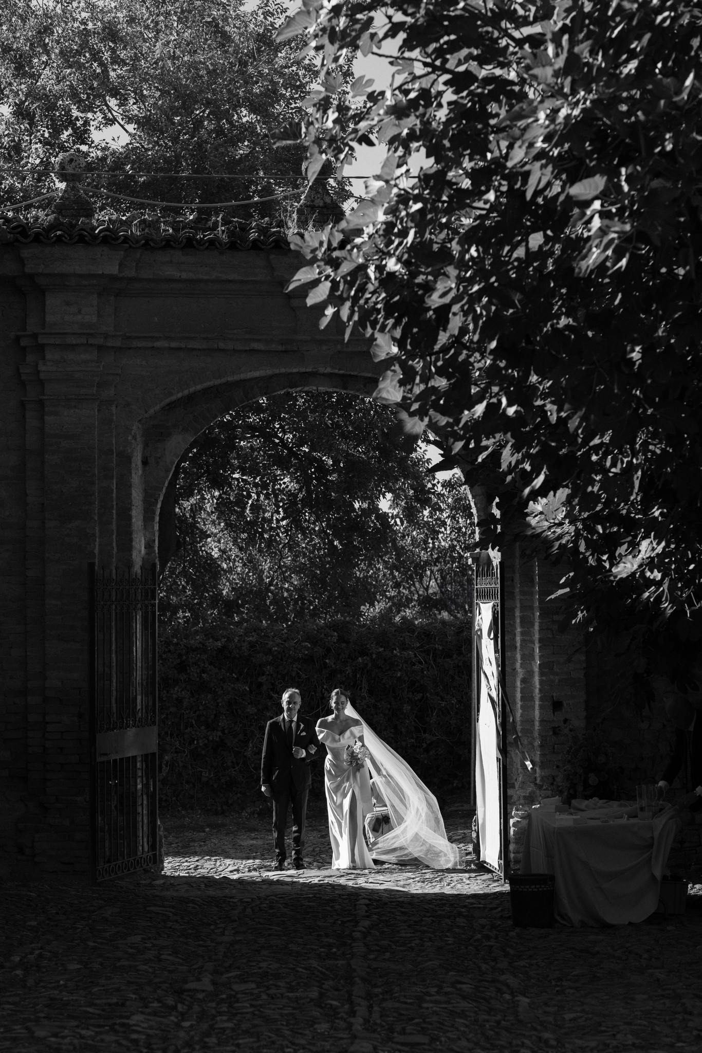 Sposi sotto l'arco in pietra del Castello di Scipione, abito illuminato dalla luce naturale nel reportage matrimoniale