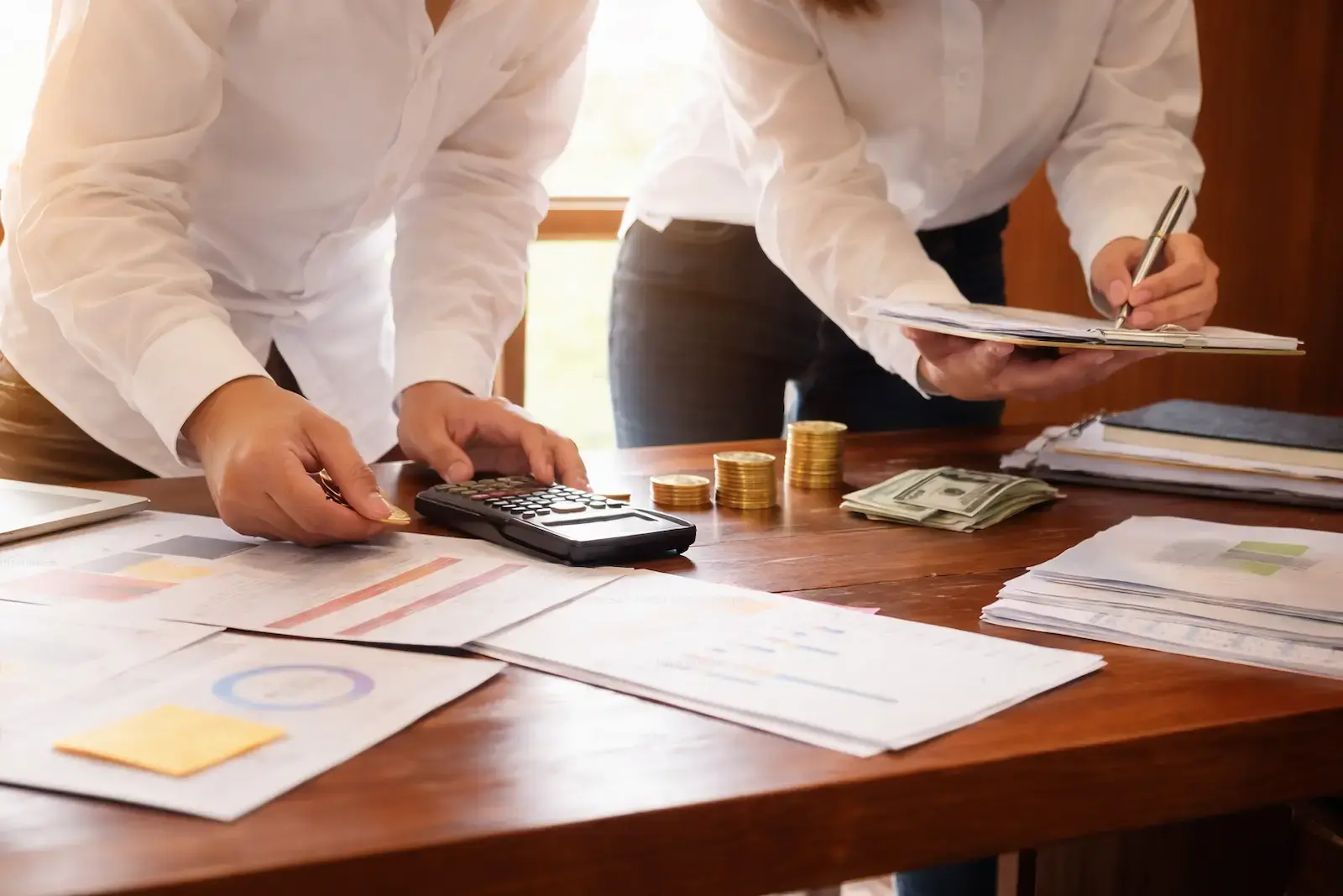 People reviewing finances at a desk with documents, cash, coins, and a calculator.
